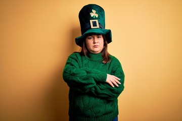 Young beautiful plus size woman wearing green hat with clover celebrating saint patricks day skeptic and nervous, disapproving expression on face with crossed arms. Negative person.