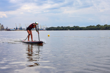 Young girl-surfer with perfect body on stand-up paddle board SUP boarding on Danube river at summer day