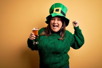 Young beautiful plus size woman wearing green hat celebrating st patricks day drinking beer screaming proud and celebrating victory and success very excited, cheering emotion