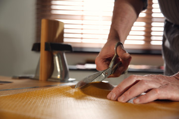Man cutting leather with scissors in workshop, closeup