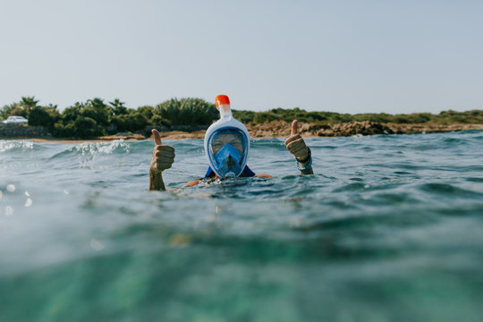 Woman at water surface wearing snorkel mask with thumbs up. Woman snorkelling in the sea on vacation facing camera and gesturing.