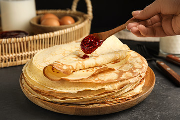Woman putting jam on stack of fresh thin pancakes at black table, closeup