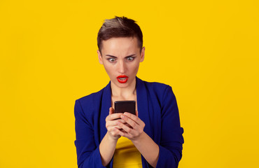 Shocked woman looking at phone. Woman shocked by the bad news she saw on the cell mobile phone. Multicultural Latina girl short hair red lips blue suit yellow shirt isolated yellow background wall