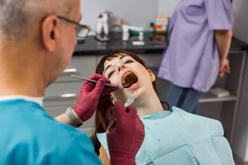 Young pretty woman patient in dental clinic having dental check and treatment, woman with open mouth, professional dentist team, senior male dentist and his female assistant