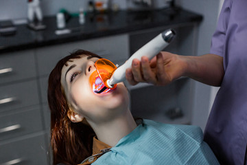 Young woman patient having dental treatment at dentist's office. Dentist using dental treatment with dental curing UV lamp on the patient's teeth