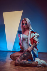 Sexy attractive woman in sunglasses and jacket is sitting on the floor.