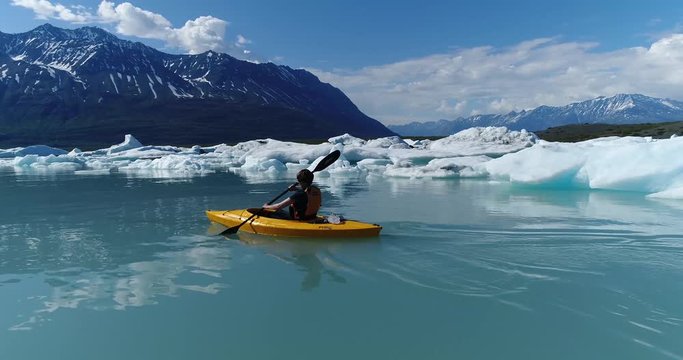 Woman kayaking by icebergs in water, Alaska, USA