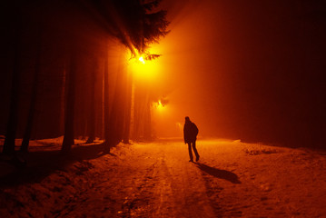 Male person silhouette in dark street countryside road with snow in winter