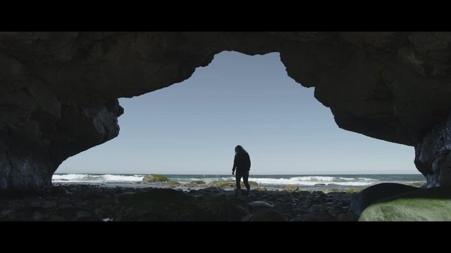 Slow motion shot of woman hiking into a cave near sea, The Arches, New Foundland, Canada