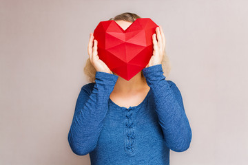 Woman holding polygonal diamond shaped red heart in front of her face