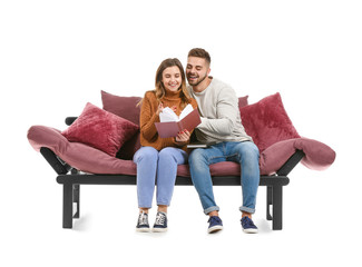 Fototapeta na wymiar Young couple reading book while sitting on sofa against white background
