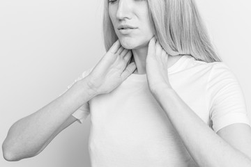 Female checking thyroid gland by herself. Close up of woman in white t- shirt touching neck with red spot. Thyroid disorder includes goiter, hyperthyroid, hypothyroid, tumor or cancer Health care.