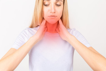 Female checking thyroid gland by herself. Close up of woman in white t- shirt touching neck with...