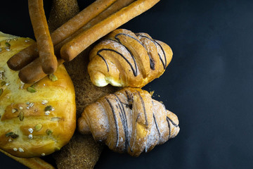Different kinds of fresh bread with grain on black rustic background.