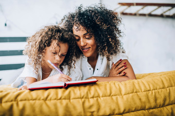 Black mother and daughter lying in bed and writing in journal together
