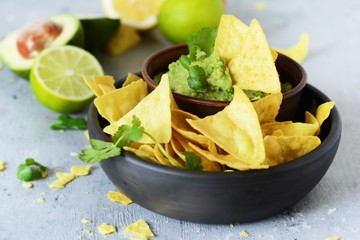 Bowl of guacamole dip with corn  nachos (chips) and ingredients on a blue background, selective...