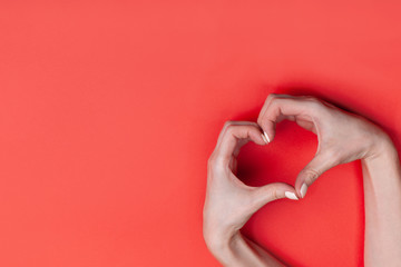 Female hands show a heart symbol on a red background. Place for text, copy space.