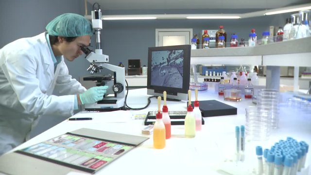 Lockdown, MS of a lab tech looking into a microscope connected to a monitor 