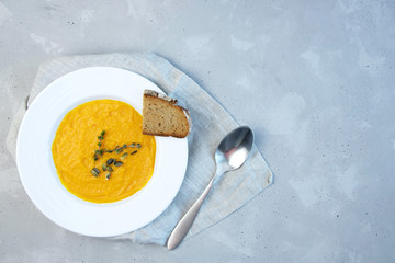 Pumpkin cream soup in a white porcelain plate on a gray table, decorated with a slice of bread and a sprig of rosemary. Copy space