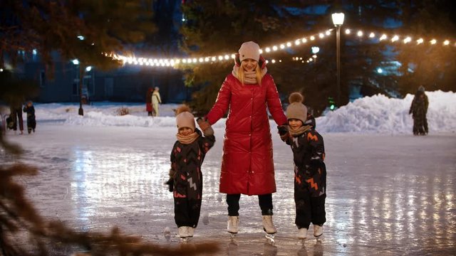A family of young mother and two kids skating on the decorated ice rink