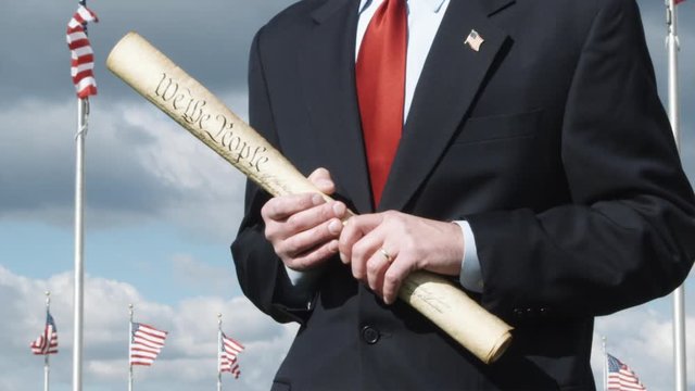 SLO MO, CU of man holding a rolled up Declaration of Independence in front of American flags