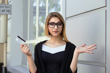 Confused stressed woman showing credit card in one hand, gesturing i don't know, so what with other...