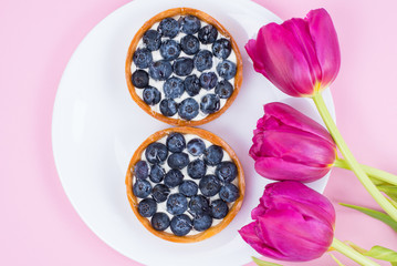 Happy women's day concept. Top flat lay flatlay above view photo of beautiful bright flowers and two delicious tarts with sweet blueberries isolated pastel soft color background