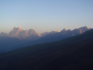 Mountain landscape of Svaneti on bright summer sunny day. Mountain lake, hills covered green grass on snowy rocky mountains background. Caucasus peaks in Georgia. Amazing view on wild georgian nature