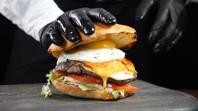 Male chef hand pressing juicy burger dripping sauce and yolk in slow motion. American Burger with Egg and fresh vegetables, served in restaurant, close-up view, Full hd