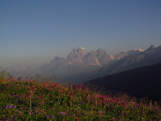 Mountain landscape of Svaneti on bright summer sunny day. Mountain lake, hills covered green grass on snowy rocky mountains background. Caucasus peaks in Georgia. Amazing view on wild georgian nature
