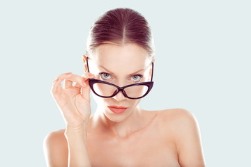 Skeptical. Closeup portrait beautiful young woman, lady looking at you camera over glasses gesture skeptically, isolated light blue background. Negative human emotions, facial expression body language