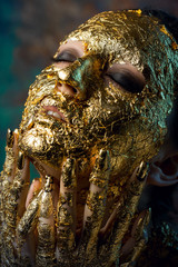 Girl with a mask on her face made of gold leaf. Gloomy studio portrait of a brunette on an abstract background.