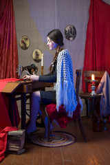 Teenaged girl dressmaker using antique sewing manual machine. Girl in a chalet in retro style in a faint candlelight.