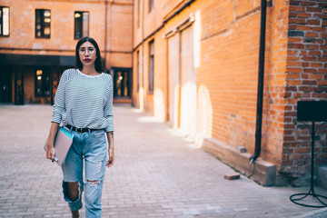Confident woman walking with laptop in urban yard