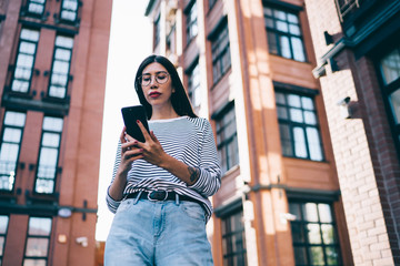 Fototapeta premium Millennial female blogger using 4g tariff with unlimited internet access for networking social websites and sharing content news to followers, Latino woman in classic glasses texting via application