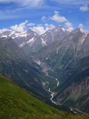 Mountain landscape of Svaneti on bright summer sunny day. Mountain lake, hills covered green grass on snowy rocky mountains background. Caucasus peaks in Georgia. Amazing view on wild georgian nature