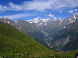 Fototapeta premium Mountain landscape of Svaneti on bright summer sunny day. Mountain lake, hills covered green grass on snowy rocky mountains background. Caucasus peaks in Georgia. Amazing view on wild georgian nature