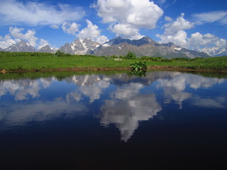 Mountain landscape of Svaneti on bright summer sunny day. Mountain lake, hills covered green grass on snowy rocky mountains background. Caucasus peaks in Georgia. Amazing view on wild georgian nature