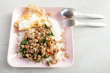 Rice topped with stir-fried pork and basil in a white dish.