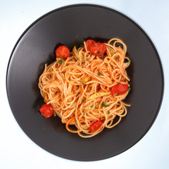 Spaghetti with tomatoes on a black plate.