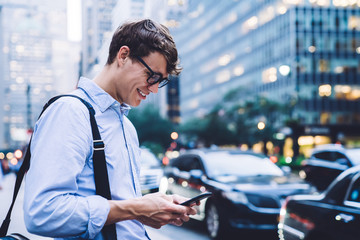 Young employee in shirt and glasses texting on phone smiling outdoors