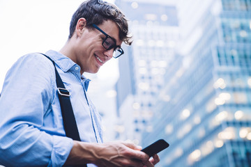 Low angle of man in glasses texting on phone at street looking happy