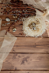 Easter quail eggs in nest and willow branch on a wooden background, copy space
