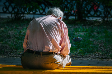 A lonely old man sitting on a bench in a park