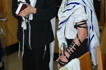 Fototapeta na wymiar Bar Mitzvah, Israel. Jewish coming of age ritual for boys. A boy during prayer with Tefillin on his arm and a Tzitzit on his shoulders