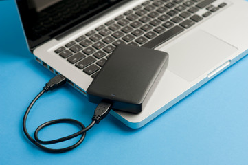 external hard drive with black cable (usb), on laptop, blue table.