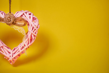 decorative pink heart made of branches with woolen thread. pendant decoration on the right on a yellow background. Valentine's Day