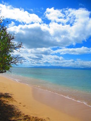 Une plage de sable blanc avec la mer calme et turquoise sous un ciel nuageux