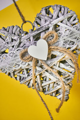 gray decorative pendant in the shape of a heart made of branches with woolen thread. decoration on a yellow background. Valentine's Day. Macro