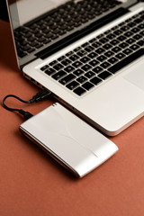 Aluminum external hard drive, partial laptop view, brown background, office concept.